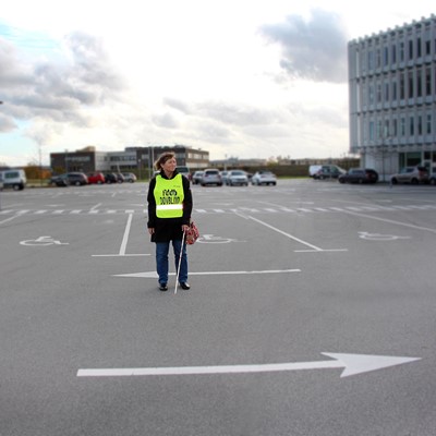 Døvblind kvinde står alene på en parkeringsplads med hvid stok