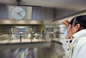 Ung døvblinde kvinde prøver at se klokken på et ur på en metrostation. Omgivelserne er slørede