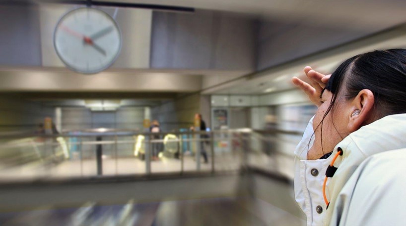 Ung døvblinde kvinde prøver at se klokken på et ur på en metrostation. Omgivelserne er slørede