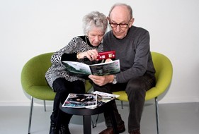 Ældre døvblind kvinde læser i en pjece vha lup - hendes ægtefælle holder pjecen for hende