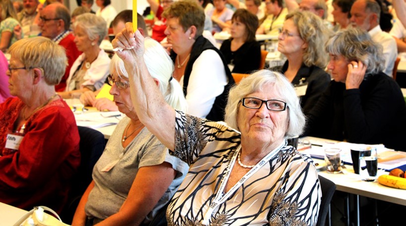 Deafblind woman is raising her hand with a yellow paper to vote on the annual assemble of FDDB 
